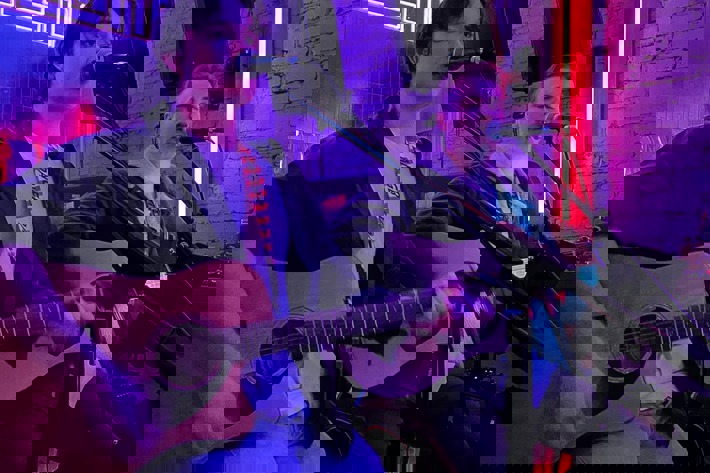 Two musicians performing with acoustic guitars under vibrant neon lighting in an intimate venue.