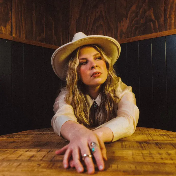 Charlie Lane sitting at table, hands out front, on table, Charlie has blonde hair and is wearing a white hat.