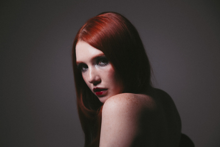 Person with red hair gazing intensely over their shoulder in soft lighting.