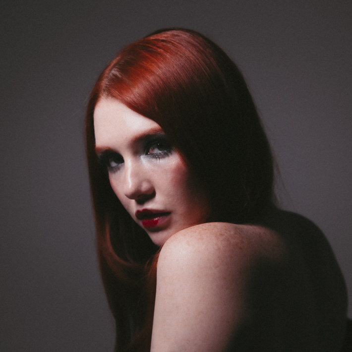 Person with red hair gazing intensely over their shoulder in soft lighting.