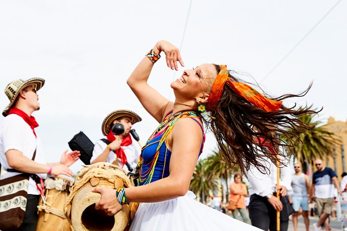 A woman energetically spinning around with hair flicking out while playing a handheld drum