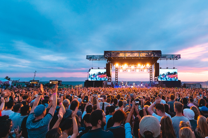A big stage in front of the bay lit up at dusk with a big crowd of people cheering