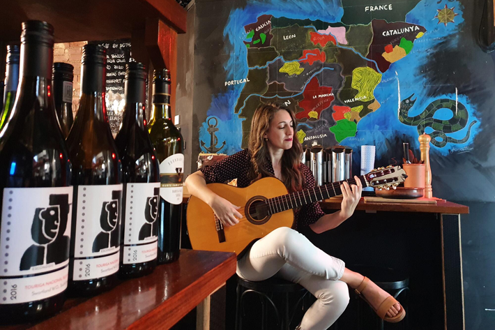 Laura de Elvira seated playing a flamenco guitar with in front of the Alhambra, a famous fortress in Granada, Spain.