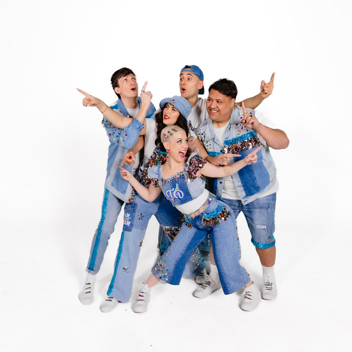 Group of five band members in bejewelled denim outfits posing energetically against a white background.