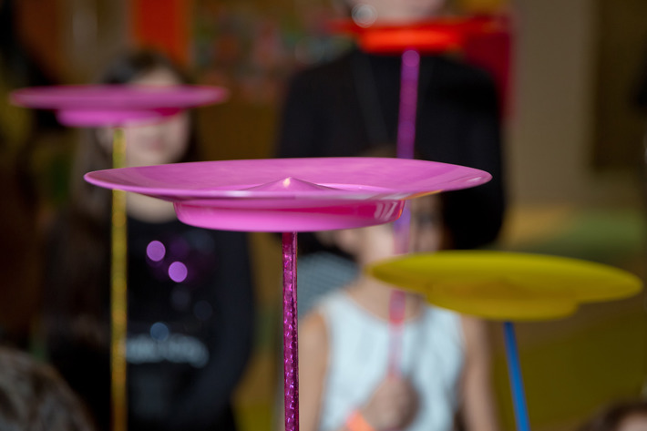 Colorful spinning plates balanced on sticks during a circus activity, with several people holding the sticks in the background.
