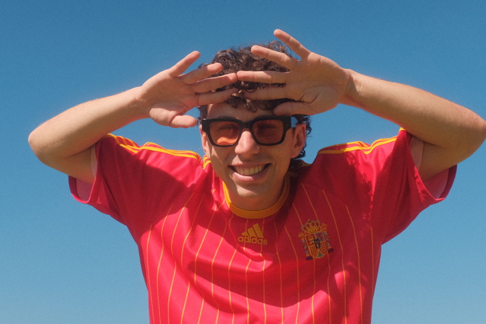 Smiling person in a red jersey and sunglasses shielding their eyes from the sun.