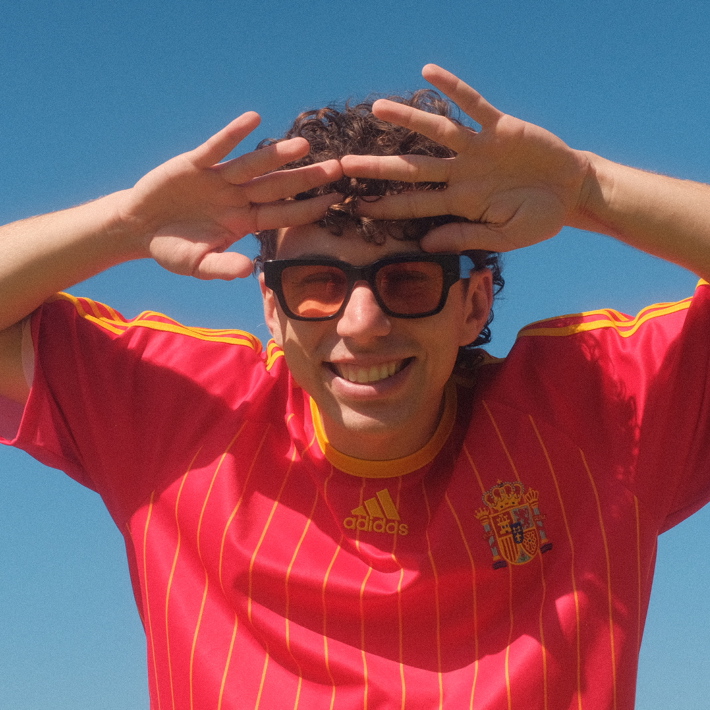 Smiling person in a red jersey and sunglasses shielding their eyes from the sun.
