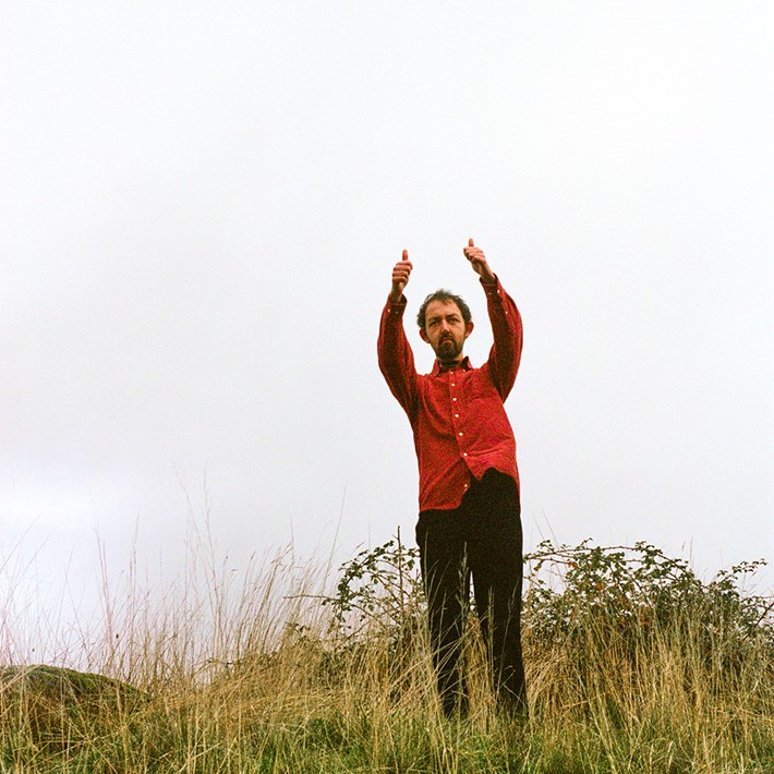 Lewis Coleman standing on a hill with his thumbs up, wearing a red shirt.
