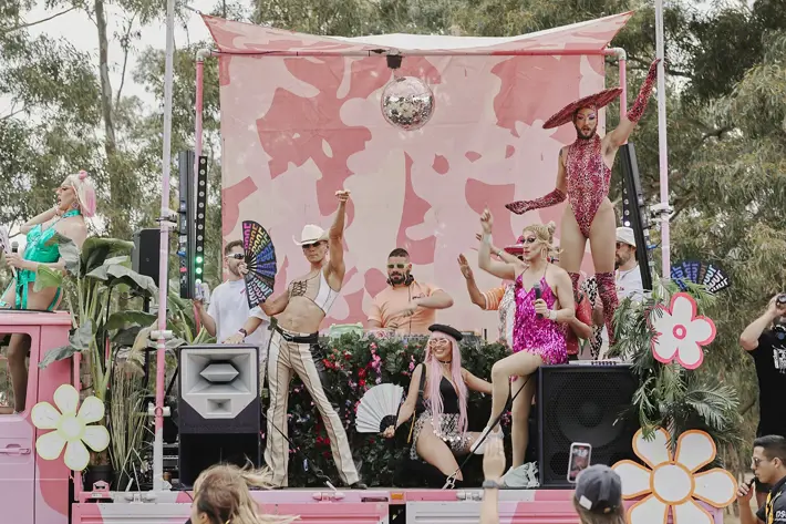 Picture of a pink army truck with various queer people dancing on the tray including a DJ and drag queens.