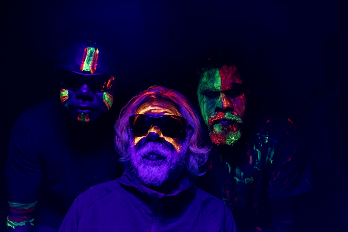 A portrait of a 3 people in UV light with intricate Indigenous paintings on their faces in bright UV light paint.