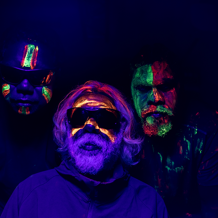 A portrait of a 3 people in UV light with intricate Indigenous paintings on their faces in bright UV light paint.