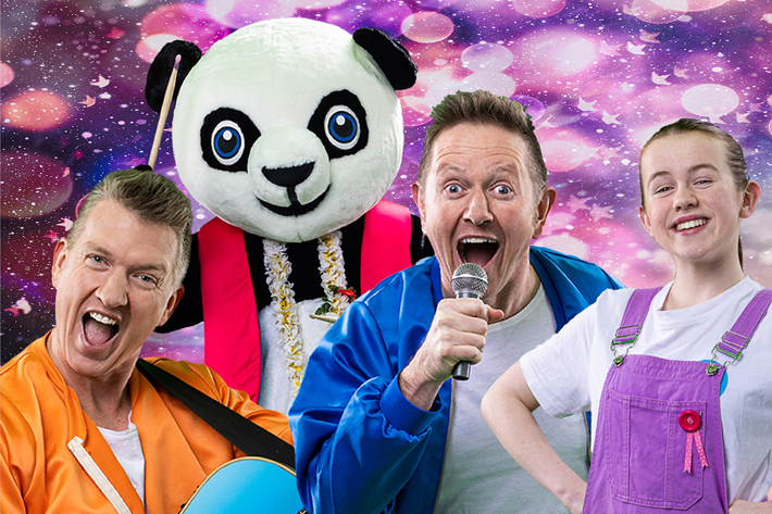 Two people wearing bright jackets, one holding a blue guitar and the other holding a microphone, standing in front of a person in a large panda costume with a floral lei. The background features a colourful, sparkling pattern with shades of pink and purple.