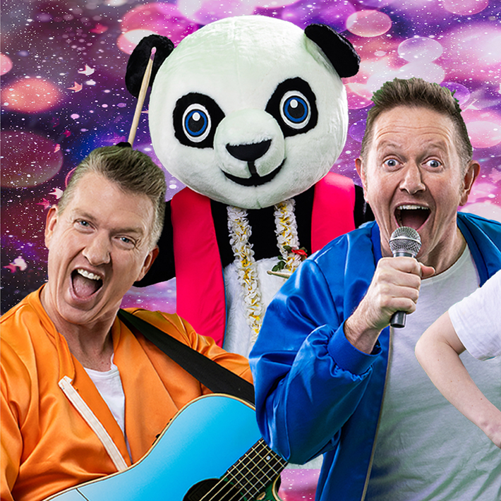 Two people wearing bright jackets, one holding a blue guitar and the other holding a microphone, standing in front of a person in a large panda costume with a floral lei. The background features a colourful, sparkling pattern with shades of pink and purple.